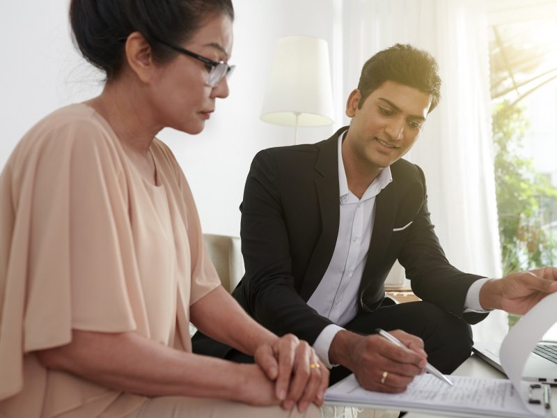 Insurance agent showing senior woman where to sign life insurance policy document