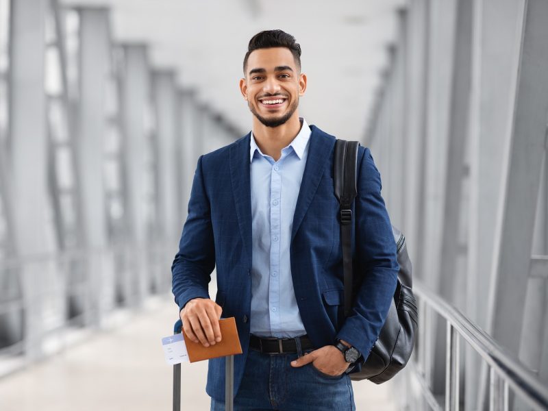 Portrait Of Young Middle Eastern Male Traveller Posing At Airport, Handsome Arab Man With Luggage, Passport And Tickets Smiling At Camera While Waiting For Flight In Terminal, Copy Space