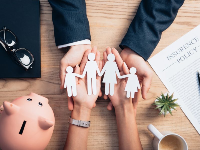 top view of lawyer and woman holding paper cut family near cup of coffee, insurance policy
